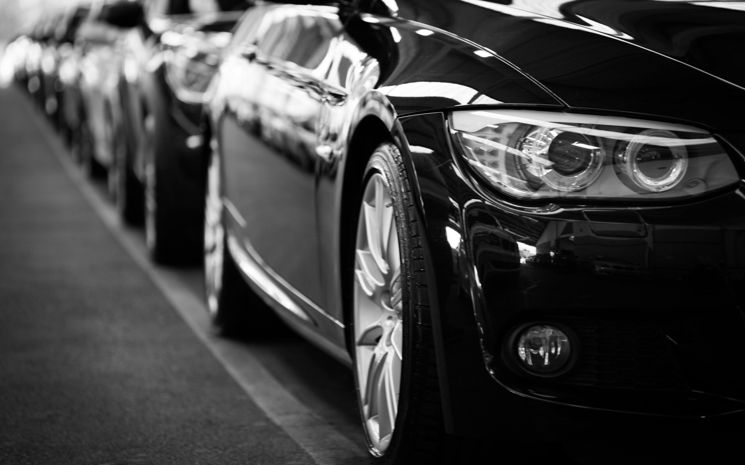 Projects Close-up black and white image of a luxury car line-up focusing on vehicle headlights.